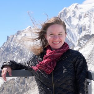 Woman with scarf and jacket smiling in front of snowy mountains