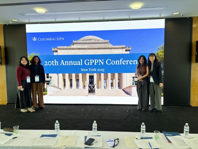 Four students stand in front of a PPT showing Columbia
