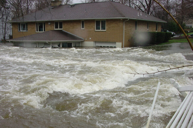 Water surrounding a half submerged yellow-brick house.