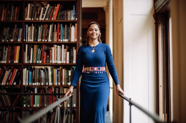 Douglass standing by a bookcase in a blue dress