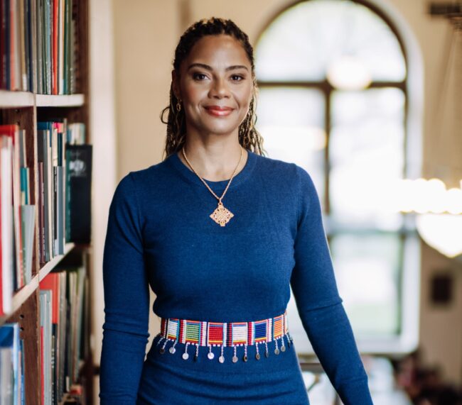 Foto Kristina Douglass berdiri di dekat rak buku