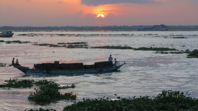 Matahari terbenam di atas sungai dengan perahu dan feri