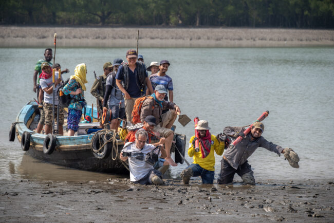 The research team dragging a boat along a muddy river 