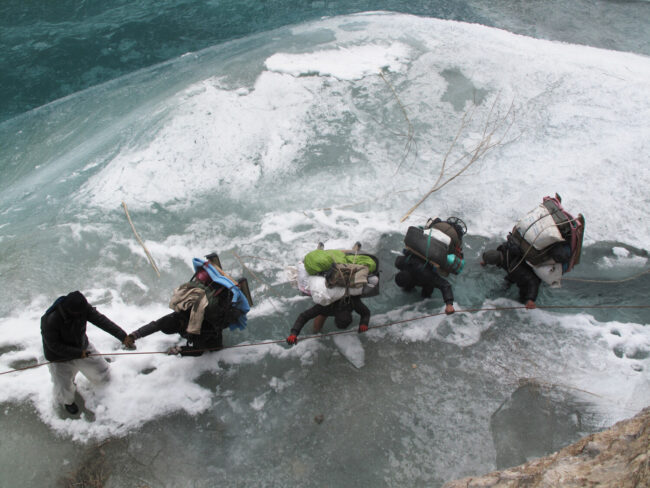 Viewed from above, five porters traverse a dangerous section, clutching onto a rope
