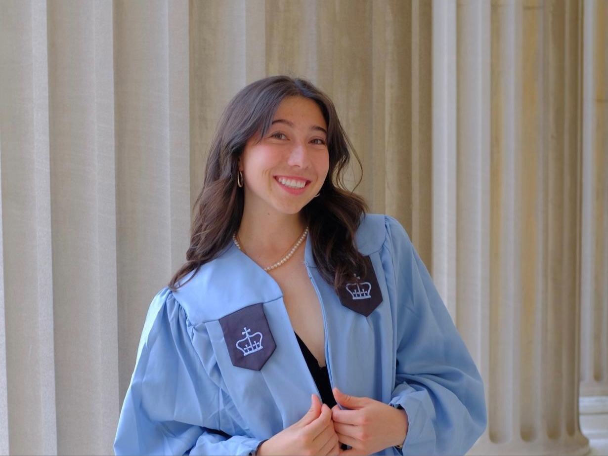 A photo of Carissa O'Donnell in a blue graduation gown in front of white columns