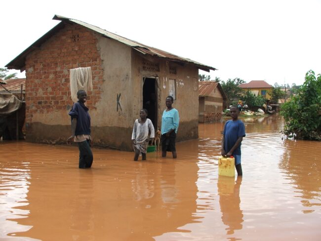 Boys standing in knee-deep murky water in front of a shack