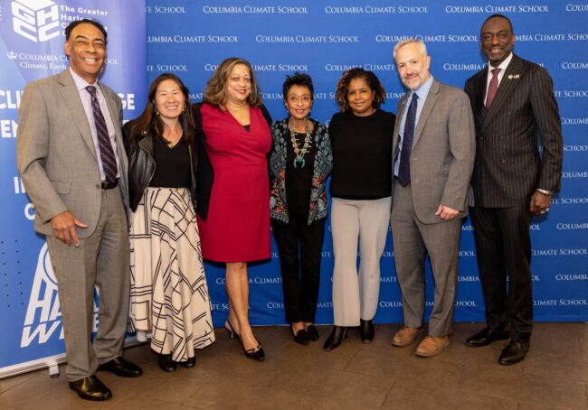 Sekelompok pembicara berdiri di depan dinding media berwarna biru 