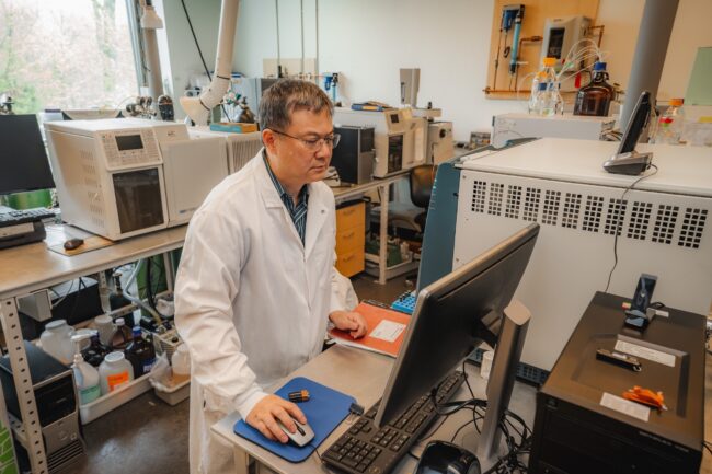 Beizhan Yan stands in a lab in front of computer 