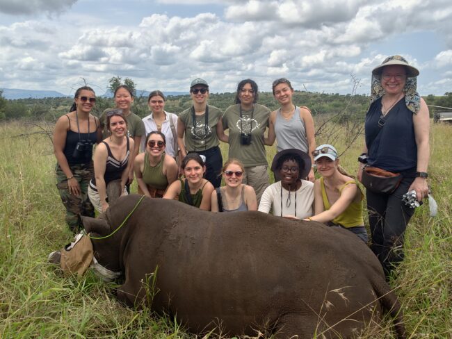 Siswa berpose dengan badak setelah prosedur pemotongan cula di Manyoni Private Game Reserve.