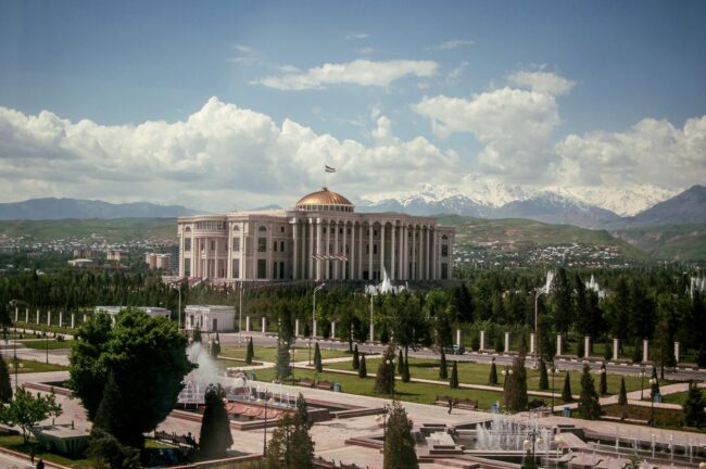 Large government building with a domed roof and fountains, set against mountains and a cloudy sky