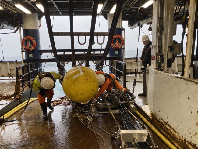 Deployment of seismic instrument aboard research ship with three crew members in hard hats