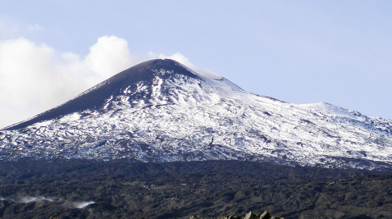 Mount Etna volcano in Sicily, Italy, with snow accumulation on its flanks. Clouds in the background.