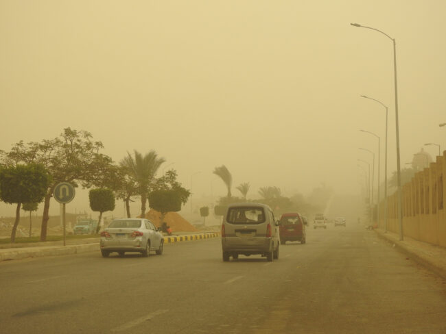 A blurry, yellowed view of cars on a highway, during a sandstorm.