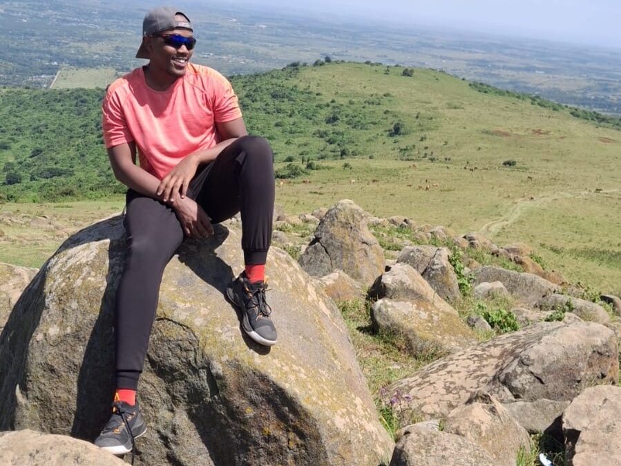 Man poses on rock in with hills behind him