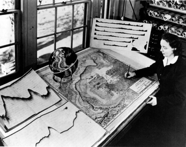 Marie Tharp at work on a map at Lamont-Doherty with scientific charts and a globe nearby, circa 1961.