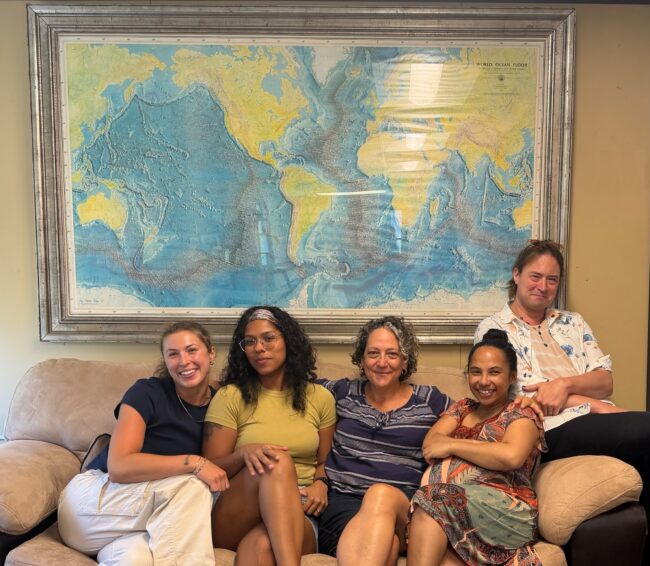 Vicki and her team sitting on a couch under a copy of the 1977 World Ocean map
