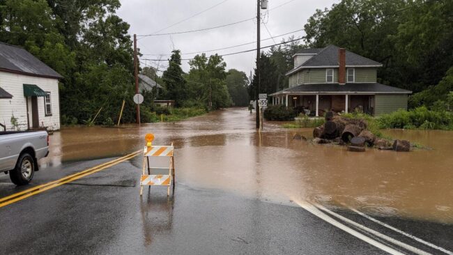 Flooded road with a house and sign blocking traffic
