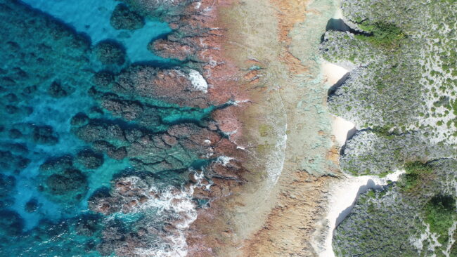 Aerial view of turquoise water, rocky reefs, and small sandy coves along a rugged coastline