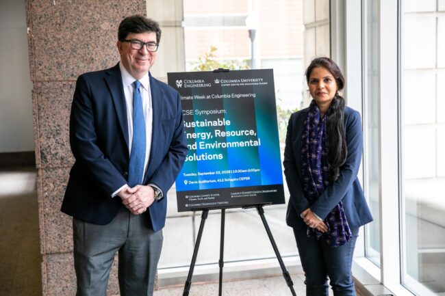Two people stand beside a Columbia University poster for a symposium on sustainable energy, resources, and environmental solutions