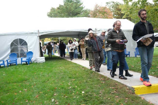 People walk along a path between large white tents at an outdoor event