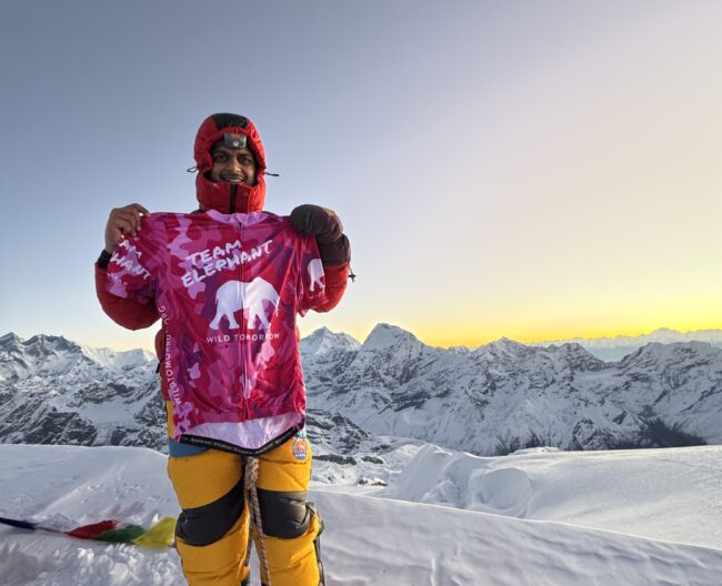 The author at Mera peak, holding up a pink shirt that says "Team Elephant"